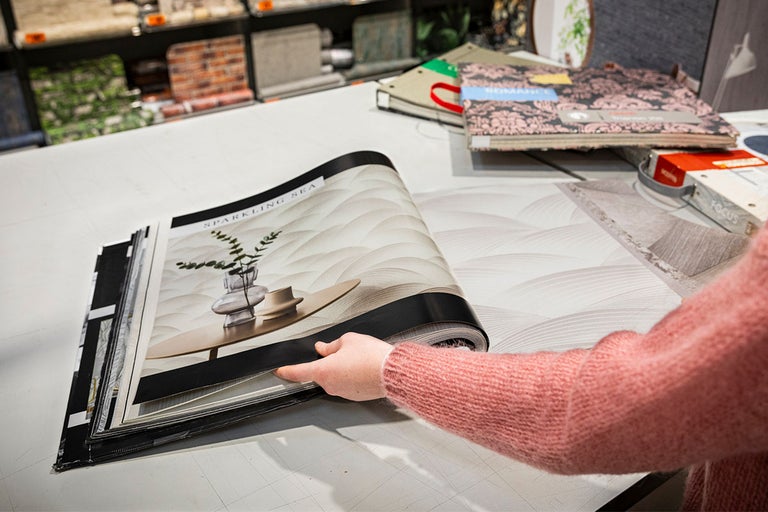 Een persoon bladert door een behangstalenboek genaamd Sparkling Sea.