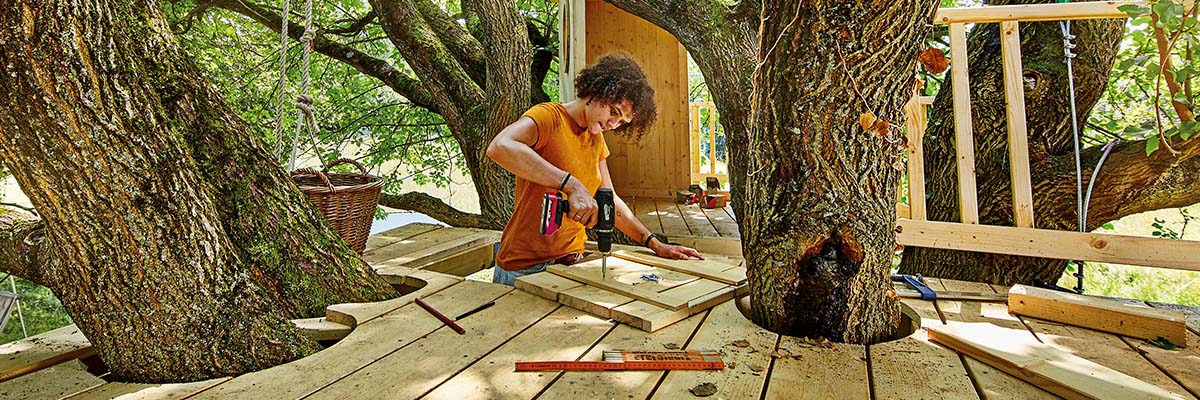 Vrouw bouwt een boomhut met een accuschroevendraaier, hout en schroeven.