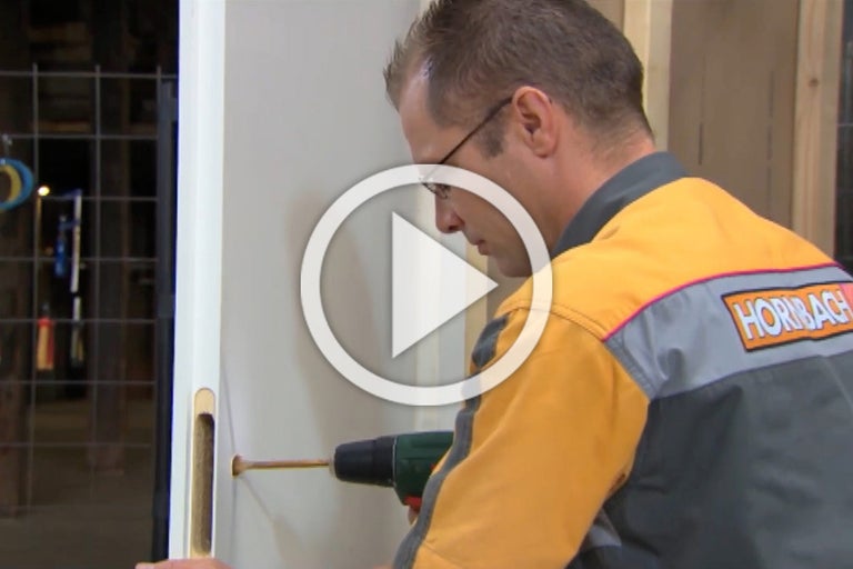 Een vakman monteert een deurslot met een accuschroevendraaier op een deur. Het Hornbach logo is zichtbaar.