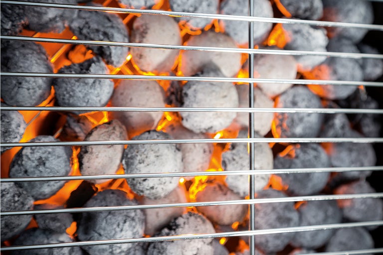 Gloeiende barbecuebriketten onder een grillrooster