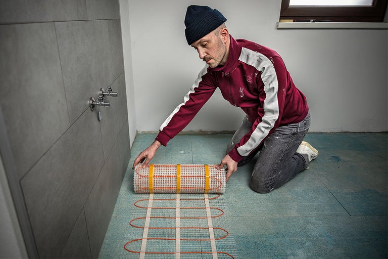Een man installeert elektrische vloerverwarming in de badkamer op de dekvloer.