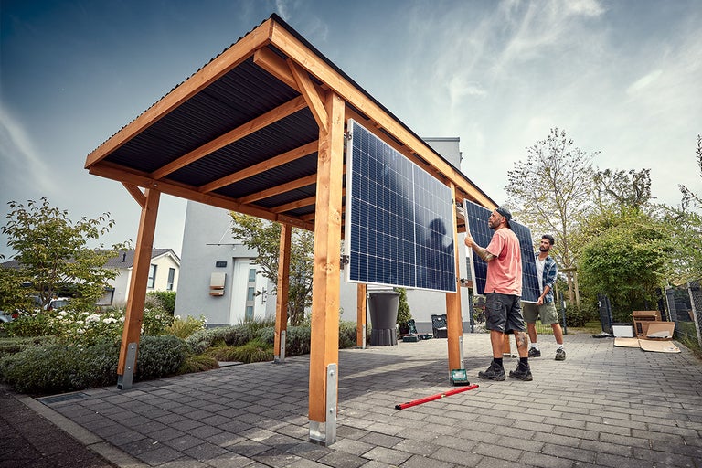 Twee mannen installeren zonnepanelen op een houten carport.