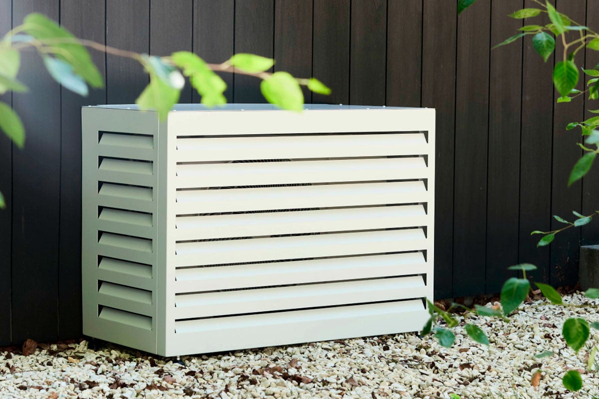 Metalen airco omkasting met lamellen geplaatst op grind voor een houten wand.