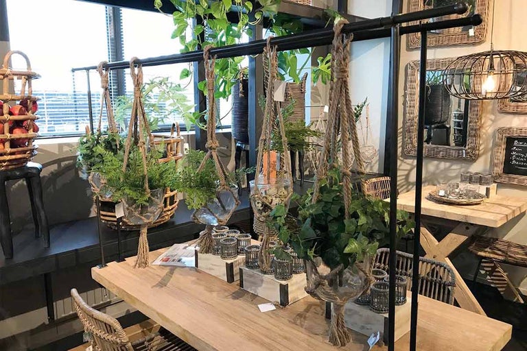 Decoratieve ruimte met hangplanten in touwhouders op een houten stang boven een houten tafel