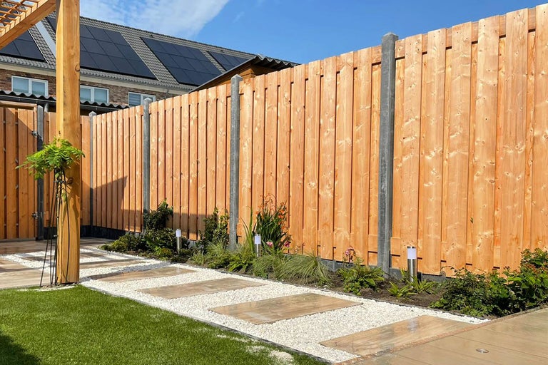 Houten schutting met betonnen palen en stoeptegels in een tuin