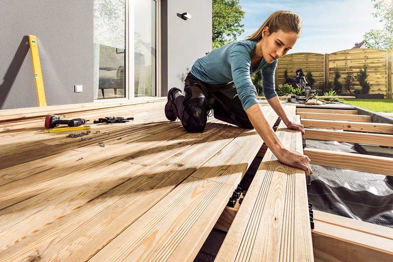 Vrouw legt een houten terras in de buitenruimte aan met gereedschap en bevestigingsmateriaal