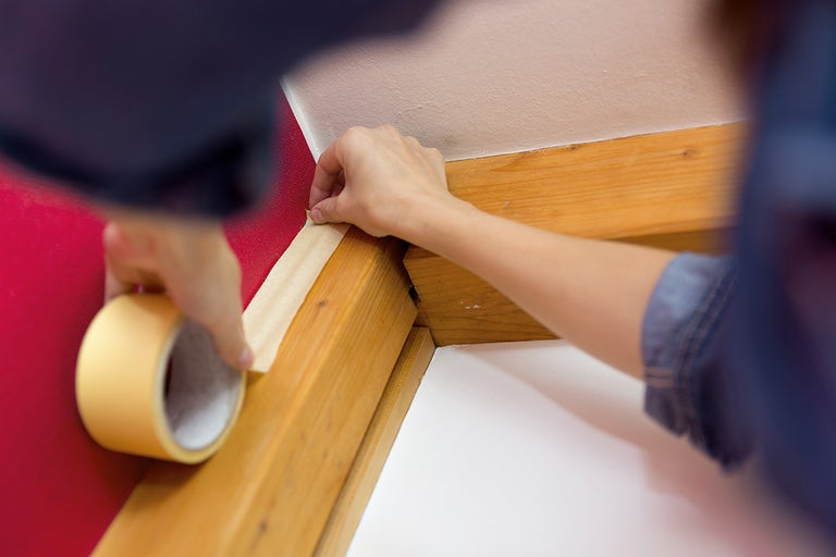 Persoon plakt schilderstape op houten lat tegen de muur