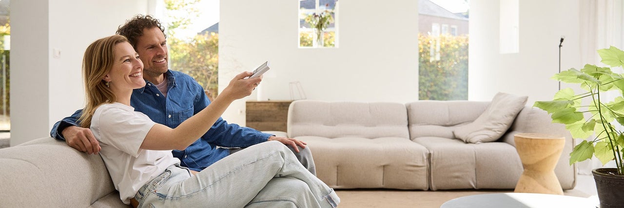 Een stel zit op een bank in een lichte woonkamer en bedient een elektronisch apparaat