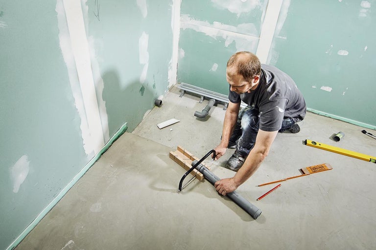 Man zaagt plastic buis met een zaag in een badkamer in aanbouw