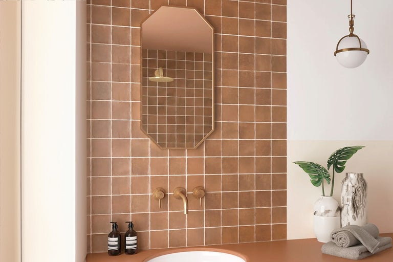 Lichte badkamer met bruine vierkante wandtegels, spiegel, wastafel en accessoires.