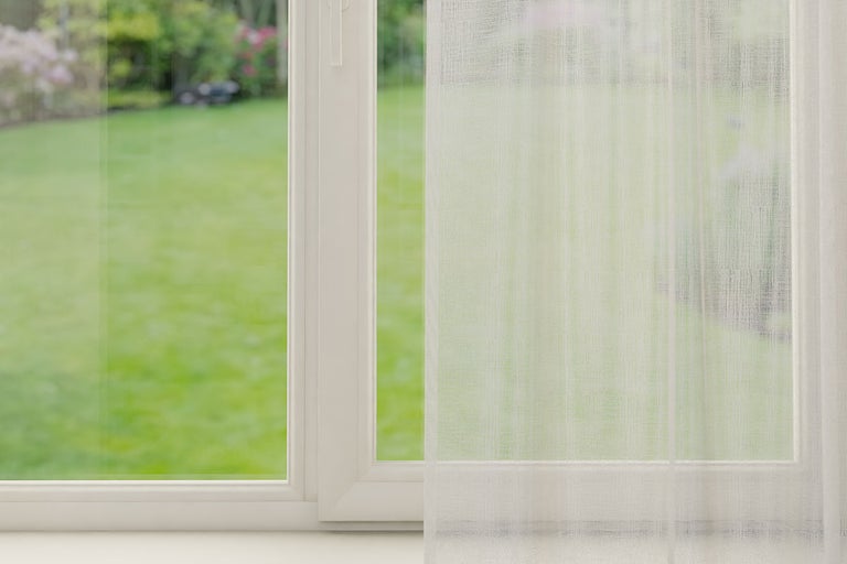 Raam met transparant gordijn en uitzicht op de tuin