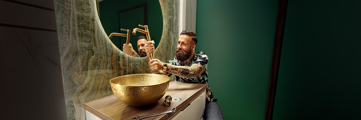 Een loodgieter installeert een kraan op een gouden wastafel in een badkamer.