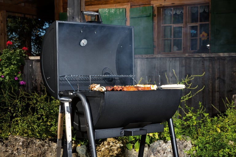 Zwarte houtskoolbarbecue met gegrild voedsel in de tuin voor een houten huis.