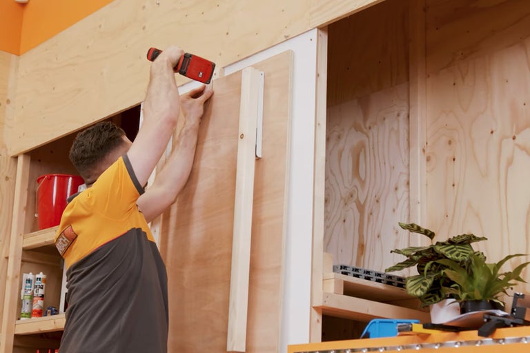 Iemand bevestigt een houten paneel aan een houten wand met een schroevendraaier.
