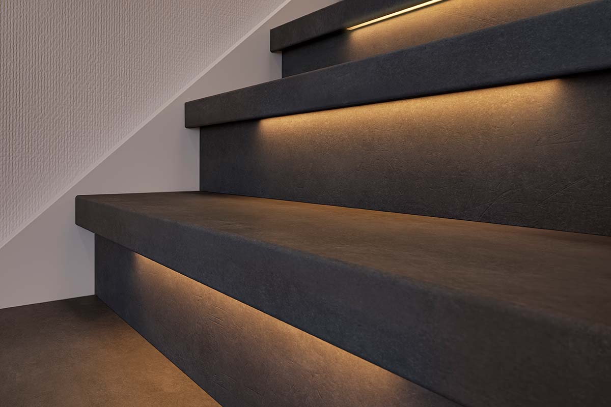 Moderne trap in donkere betonlook met indirecte, warmwitte ledverlichting onder de treden.