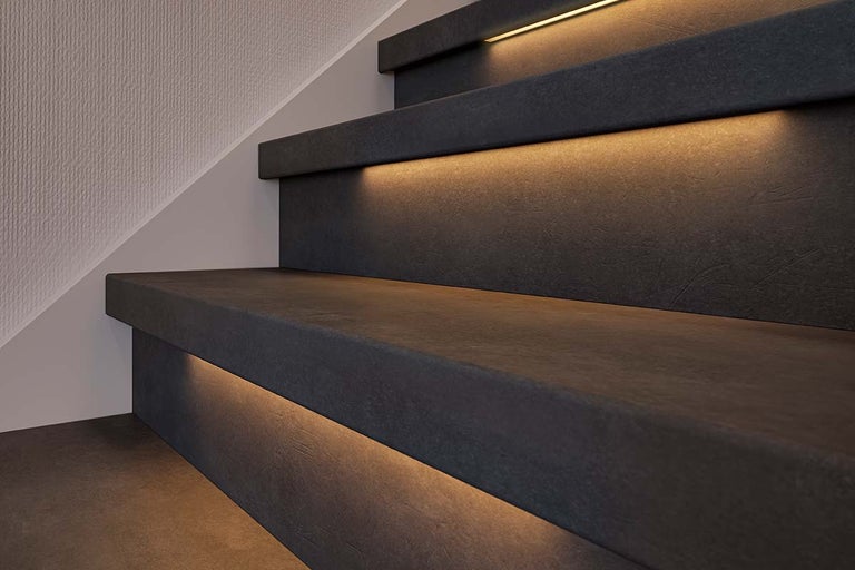 Moderne trap in donkere betonlook met indirecte, warmwitte ledverlichting onder de treden.