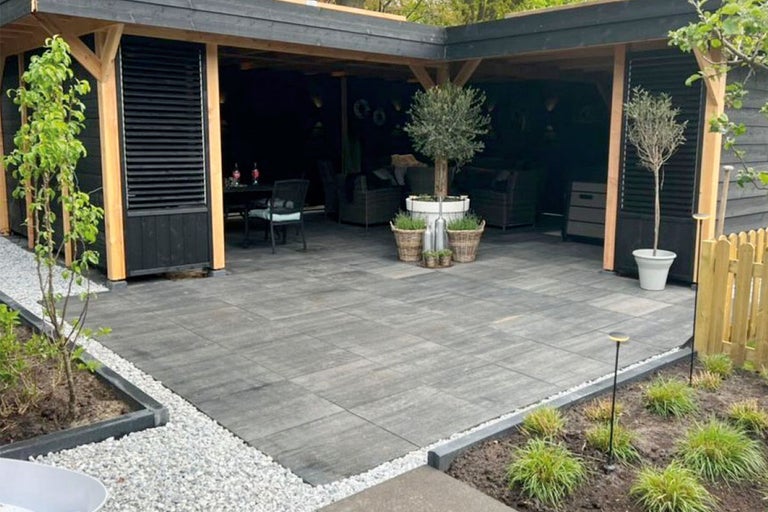 Terras met bestrating en overdekte zithoek in de tuin.
