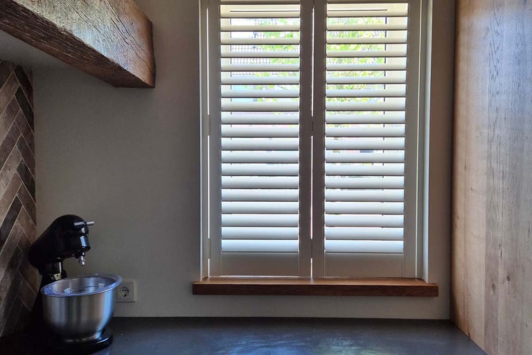 Binnenluiken met verstelbare lamellen voor een raam in een moderne keuken met houten elementen en een keukenmachine.