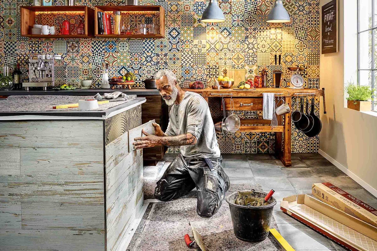 Een man legt tegels in een keuken met een betegelde achterwand in patchwork design.