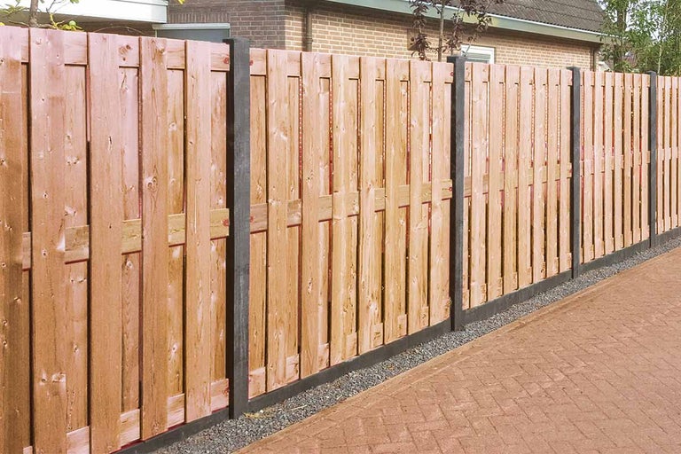 Houten schutting met verticale latten en donkere palen langs een betegeld tuinpad
