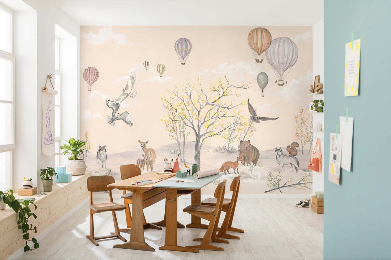 Kinderbehang met bosdieren en heteluchtballonnen in een kinderkamer met houten meubels en een lichte houten vloer.