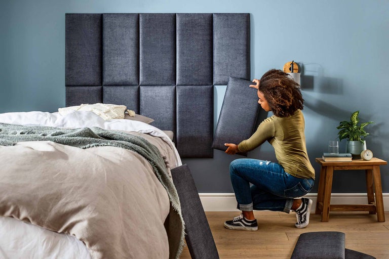 Vrouw bevestigt een gestoffeerd wandpaneel boven een bed in de slaapkamer