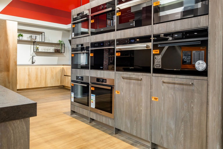 Showroomkeuken met verschillende ovens en kasten in houtlook.