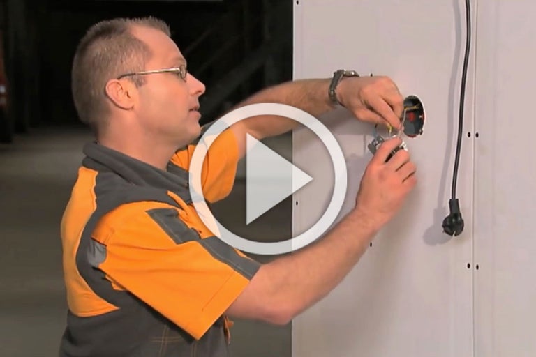 Een elektricien installeert een stopcontact in een muur.