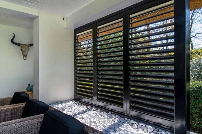 Terras met zwart lameldak, witte sierstenen en rotan stoelen