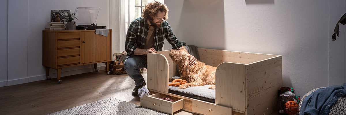 Man aait hond in een licht houten bed met lades voor hondenbenodigdheden