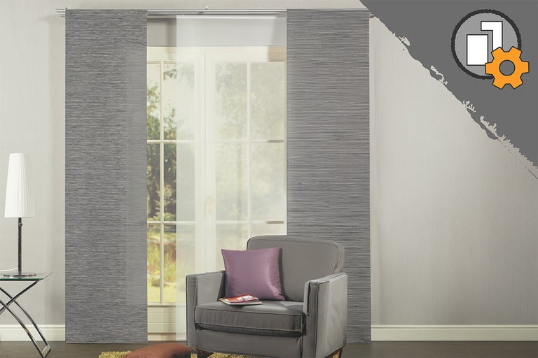 Grijze paneelgordijnen met structuur en wit transparant paneel voor een raam in een moderne kamer met fauteuil. Product individueel configureerbaar.