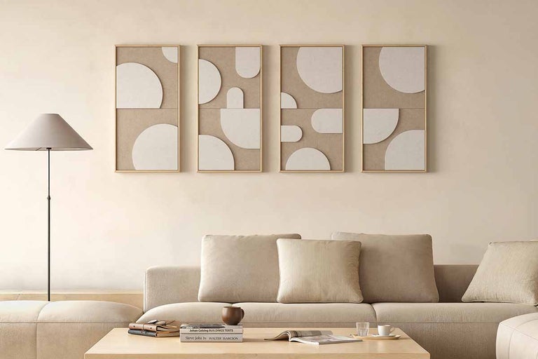 Lichte woonkamer met vier abstracte wanddecoraties in houten lijsten, een bank met kussens, een vloerlamp en een houten salontafel.