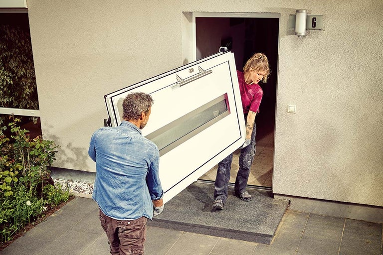 Twee mensen dragen een voordeur met glazen ruit naar een huis.