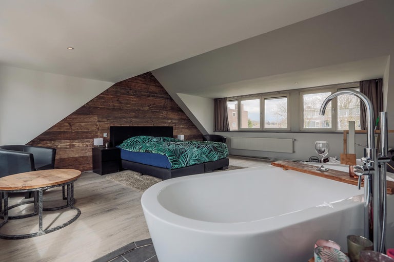 Slaapkamer met vrijstaand bad, tweepersoonsbed, houten wand en zitgelegenheid