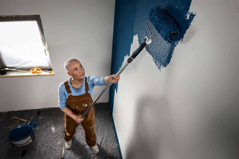 Een persoon schildert een muur met een verfroller en een telescopische stang.