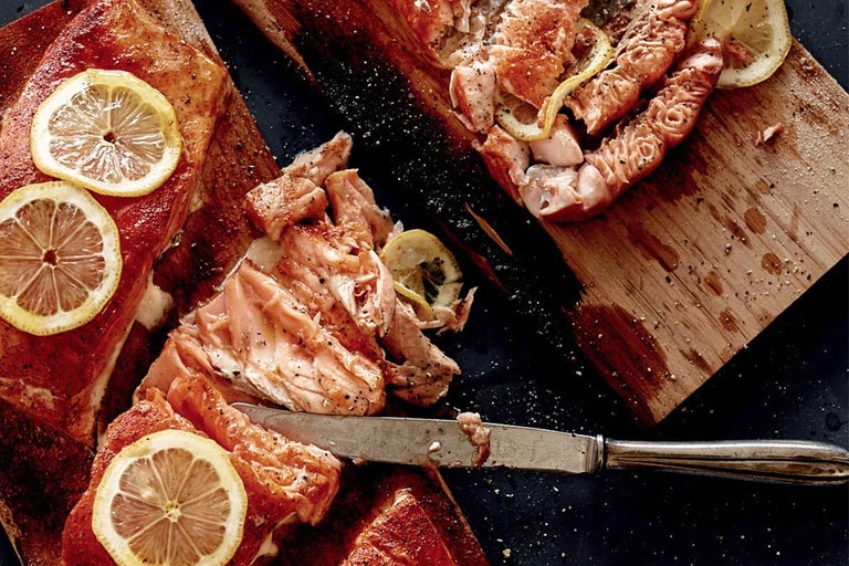 Gegrilde zalm op houten plank met schijfjes citroen en een mes.