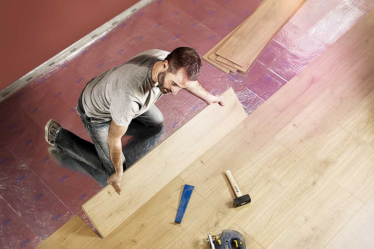Man legt laminaatvloer met gereedschap zoals een hamer en decoupeerzaag