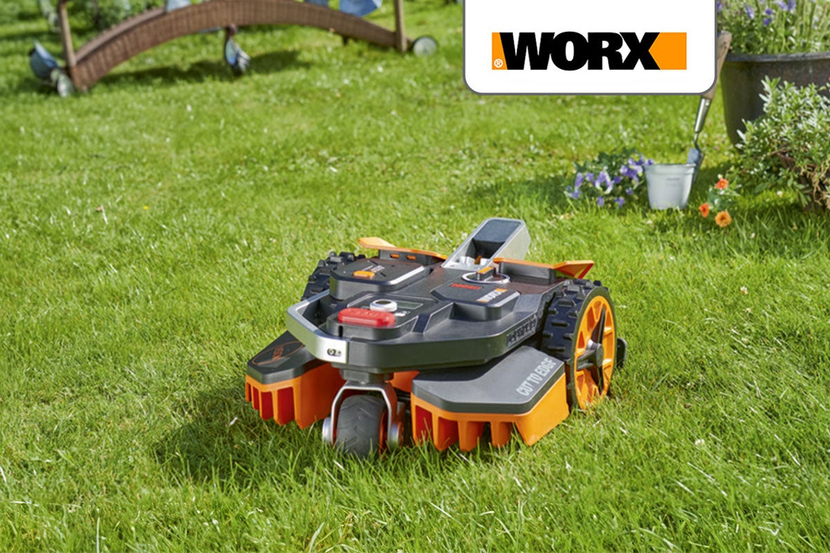 Worx robotmaaier op een gazon, omringd door tuinaccessoires en bloemen. Het Worx logo is op de achtergrond zichtbaar.
