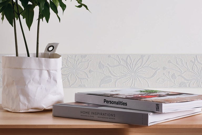Woonkamerdecoratie met een behangrand met bloemmotief op de muur, een plant in een papieren bloempot en boeken op een houten tafel.