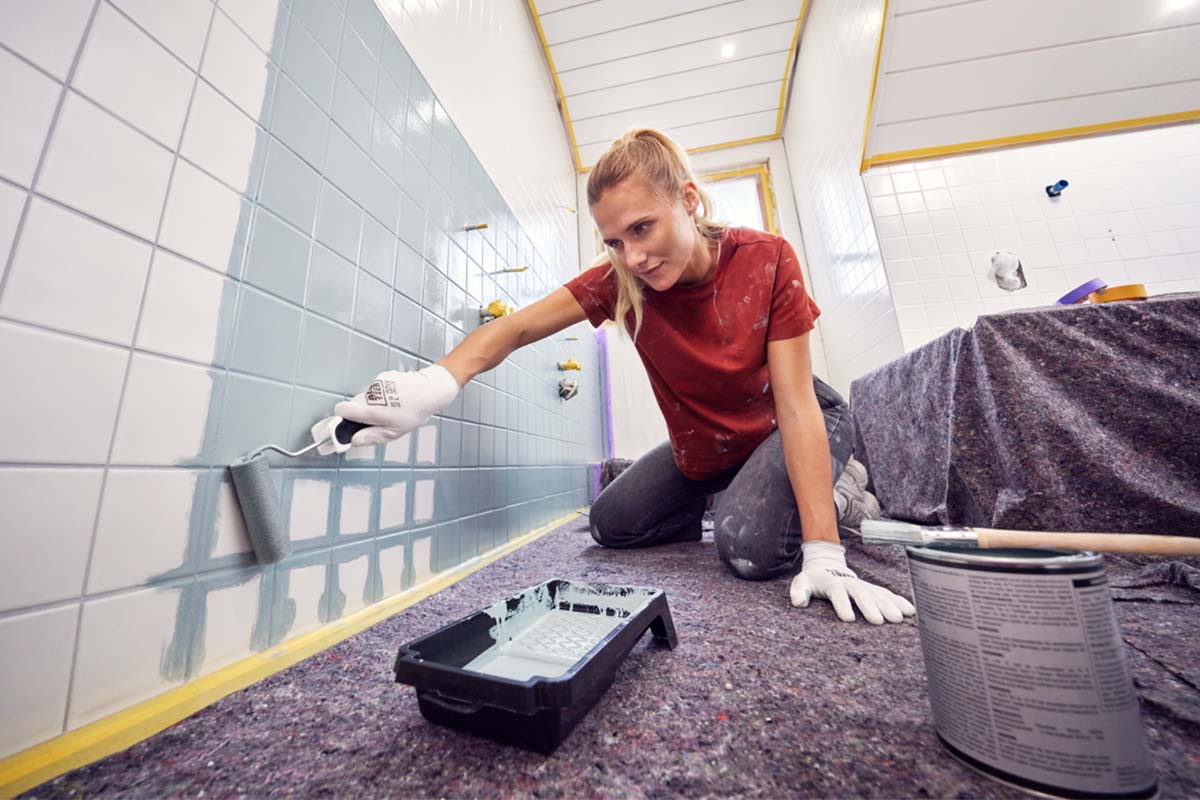 Een vrouw schildert badkamertegels met een verfroller tijdens renovatiewerkzaamheden.