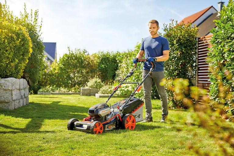 Een man maait gras met een grasmaaier in de tuin.
