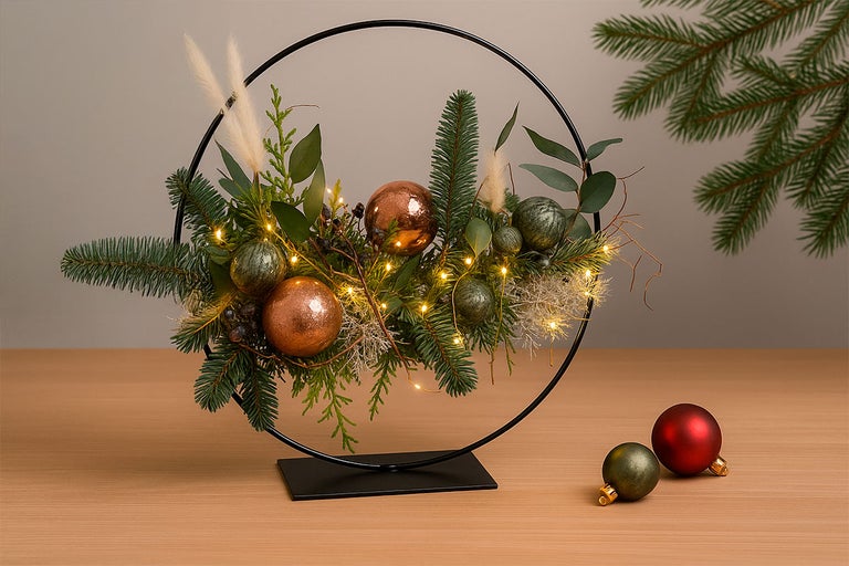 Decoratie met een zwarte metalen ring, dennenappels, bladeren, ballen en een lichtsnoer.