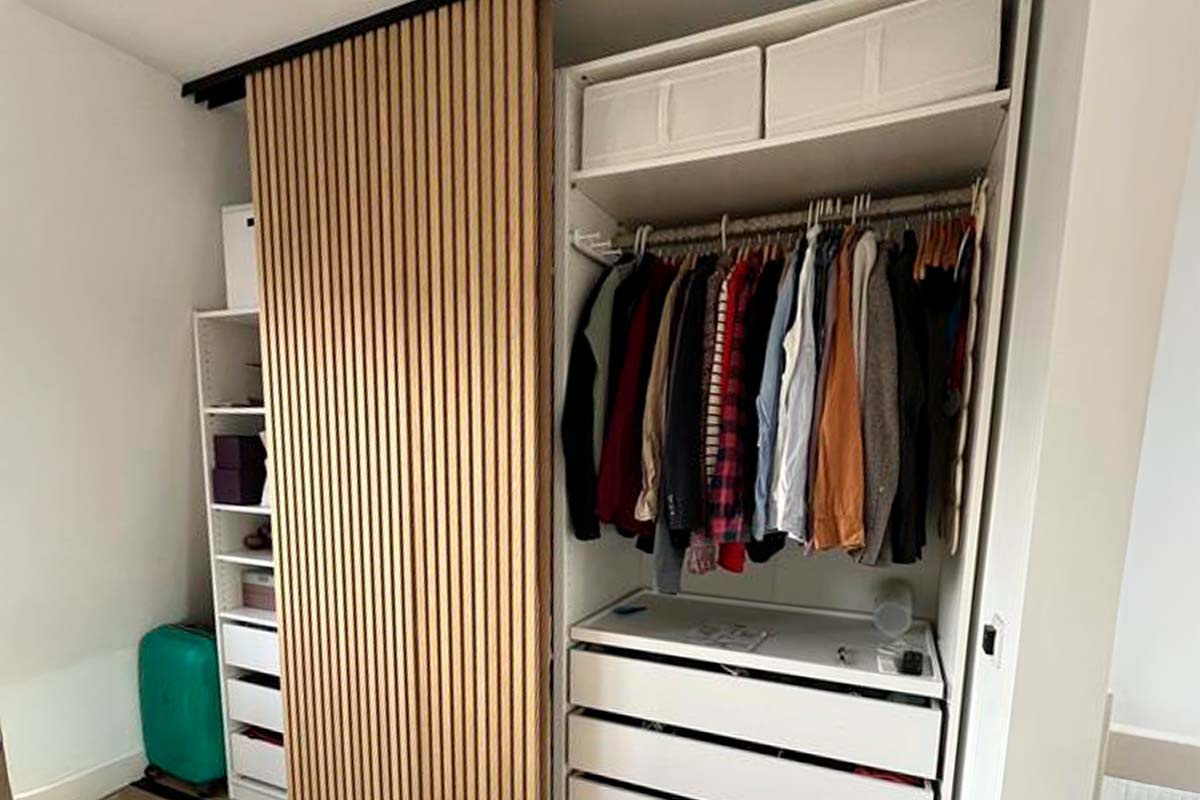 Inbouwkast met schuifdeur in lattenoptiek en open interieur met kledingroede en lades.