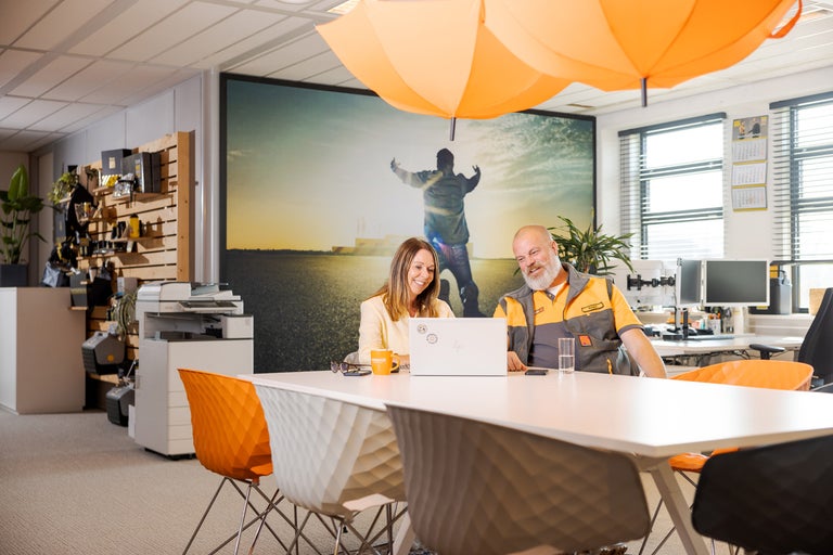 Vergaderruimte met tafel, stoelen en twee medewerkers bij een laptop