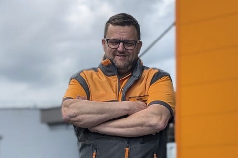 Een man met een bril en werkkleding met gekruiste armen