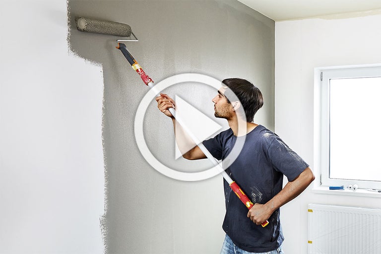 Man schildert een muur met een verfroller in een kamer