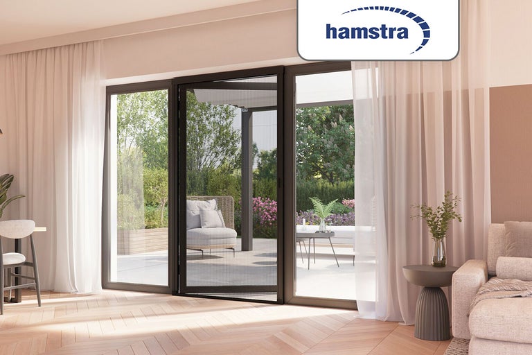 Hamstra plissé hordeur voor een terrasdeur in een lichte woonkamer met houten vloer. Hamstra Logo.