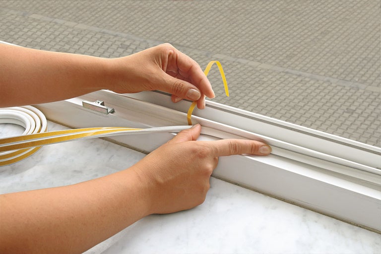 Iemand brengt afdichtband aan op een raamkozijn