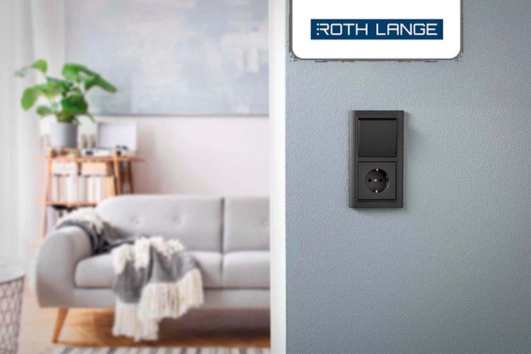 Roth Lange Logo boven een lichtschakelaar en stopcontact in een woonkamer.