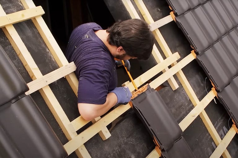 Een dakdekker werkt aan een dak met dakpannen en houten latten.